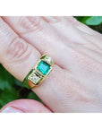 Gold ring for men with emerald and diamonds on a finger against a natural background.