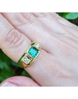 Gold ring for men with emerald and diamonds on a finger against a natural background.