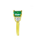 18K yellow gold three-stone ring with a rectangular Colombian emerald flanked by two trillion-cut diamonds.