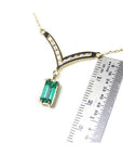 14K yellow gold necklace with a baguette-cut Colombian emerald pendant dangling from a diamond-accented curved V.