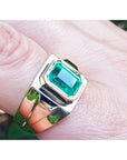 Gold ring with a bezel set solitaire emerald on a finger.