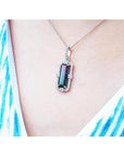 Necklace with a pendant featuring a bicolor tourmaline on a person wearing a white top with blue patterns.