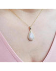 Pear-shaped Australian opal pendant with red/orange hues in 14k yellow gold on a woman's neck.