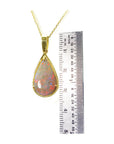 Opal pendant necklace with gold chain next to a ruler for size reference on a white background.