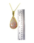 Opal pendant necklace with gold chain next to a ruler for size reference on a white background.
