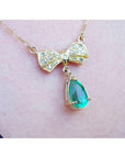 18K yellow gold bow-tie necklace with pave diamonds and a dangling pear-shaped emerald.