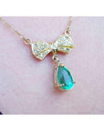 18K yellow gold bow-tie necklace with pave diamonds and a dangling pear-shaped emerald.