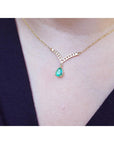 Natural pear shaped emerald necklace, is dangling from a channel set diamonds chevron design in 14k yellow gold