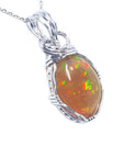 Oval Ethiopian opal pendant with vibrant play of colors and brown pinpoint fire, set in a handcrafted silver wire wrap.