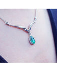A right-side view of a white gold necklace with an emerald gemstone halo diamond pendant on a person's neck