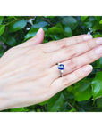 Hand wearing a sapphire ring with a green leafy background