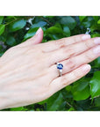 Woman's hand wearing a 14K white gold ring with a deep blue oval sapphire and side diamonds.