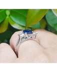 white gold ring with a blue sapphire on finger underside view against a green leafy background
