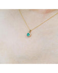 Petite round deep green Colombian emerald necklace with halo diamonds in 14k yellow gold.