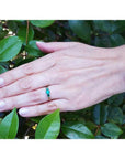 Hand wearing a round cut three stone emerald ring, 0.62 cttw, in white and yellow gold.