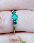 An emerald ring with round cut emeralds, Symbolizing May's birthstone, on a finger's person.
