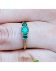 An emerald ring with round cut emeralds, Symbolizing May's birthstone, on a finger's person.