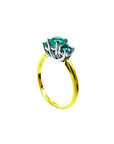 Round cut three-stone emerald ring with a yellow gold band and white gold prong setting.