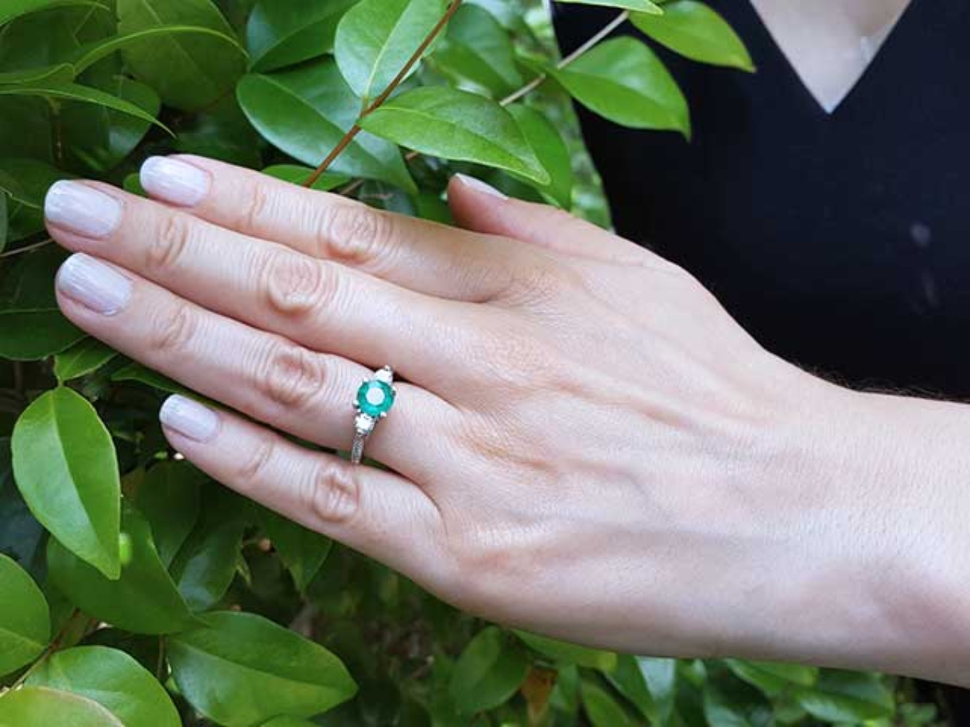 Hand wearing a real Colombian emerald ring against a green leafy background.