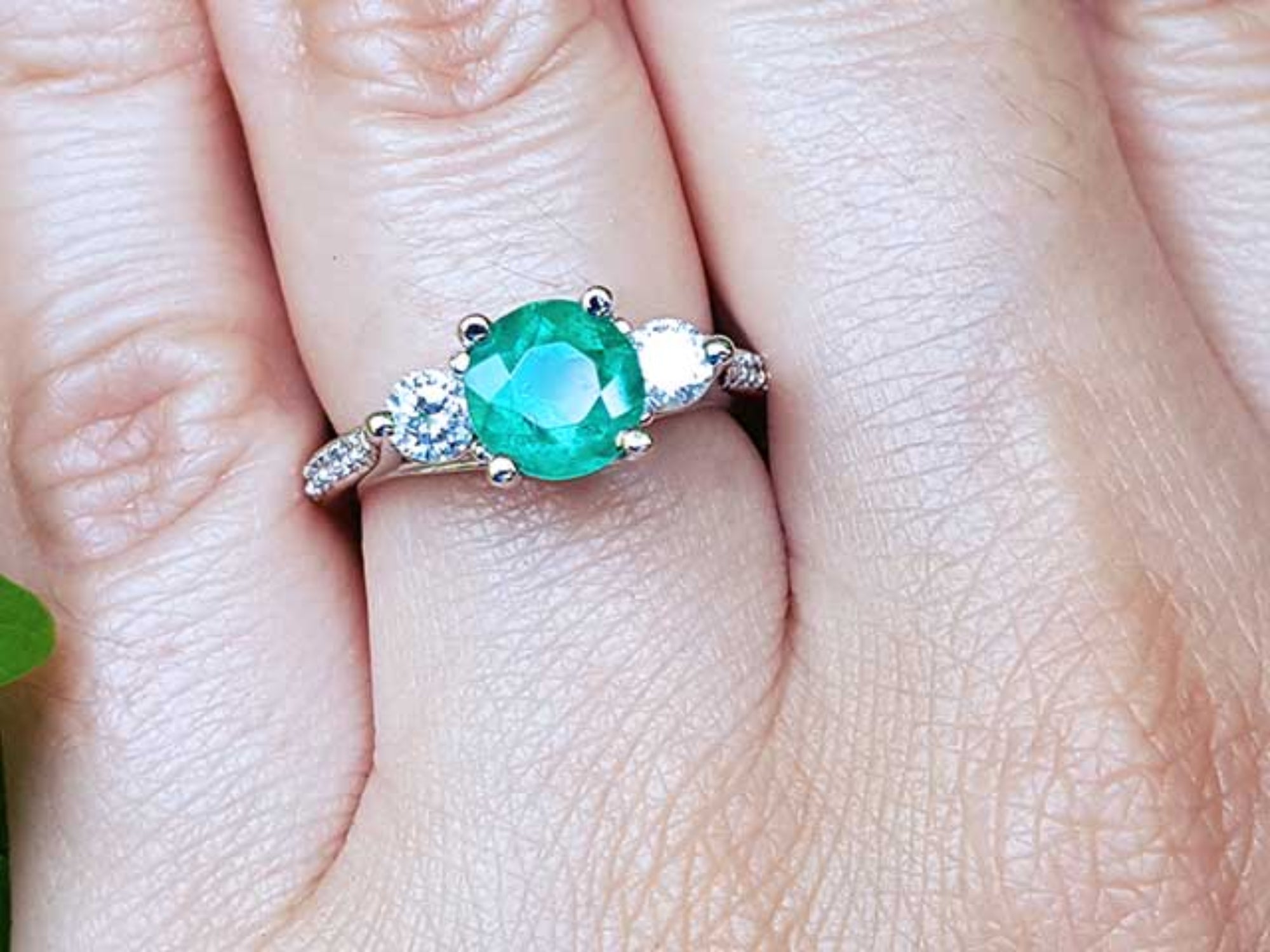 Close-up of a hand wearing an emerald ring with a diamond on a finger.