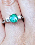 Close-up of a hand wearing an emerald ring with a diamond on a finger.