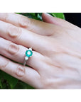 Round cut emerald ring with side diamonds in 14K white gold on a hand.