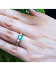 Round cut emerald ring with side diamonds in 14K white gold on a hand.