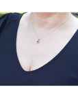 Petite round cut deep green Colombian emerald necklace with halo diamonds in 14k yellow gold on a woman's neck.