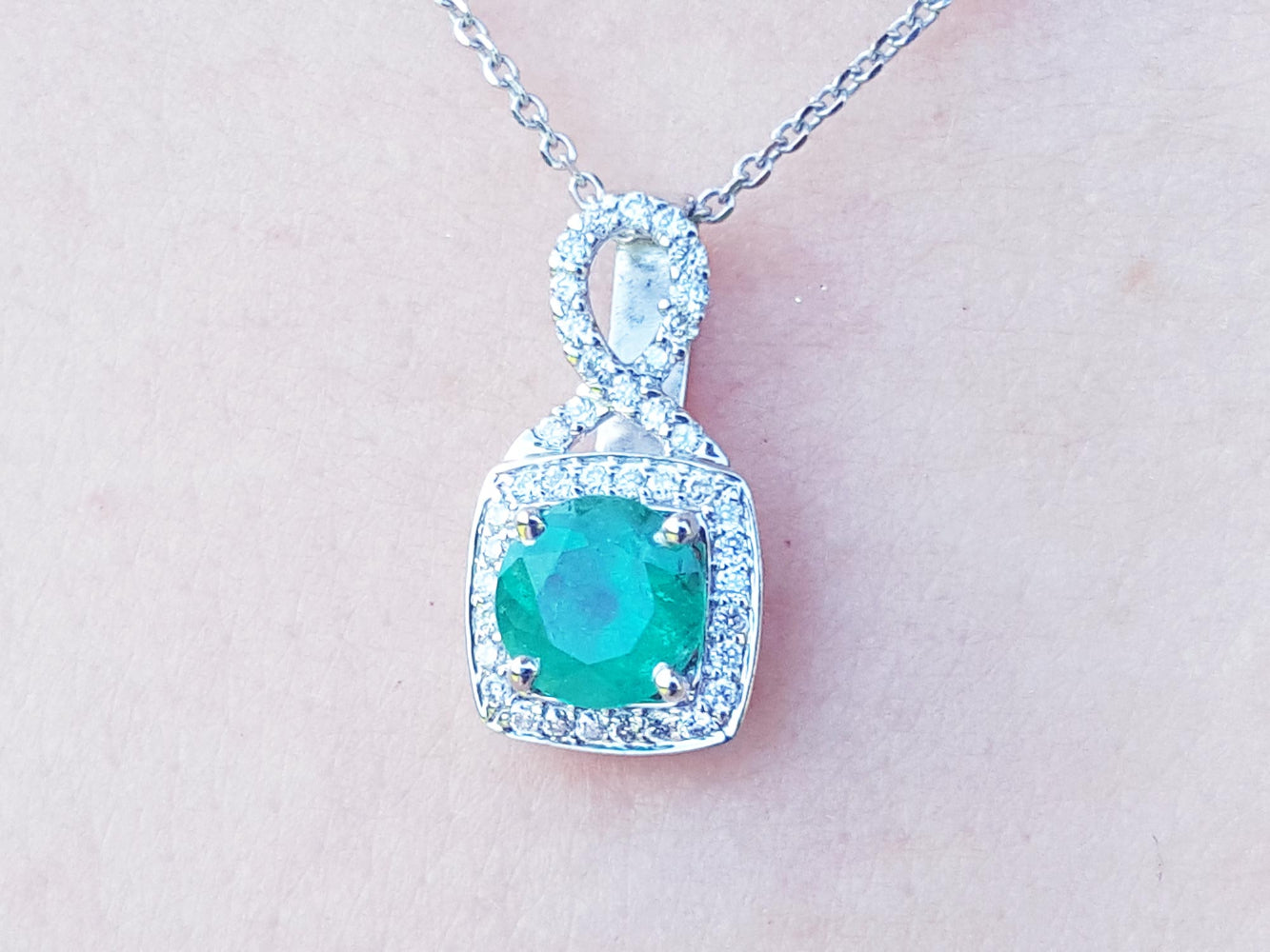 A round cut natural emerald pendant with white gold chain on a light pink background.