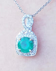 A round cut natural emerald pendant with white gold chain on a light pink background.