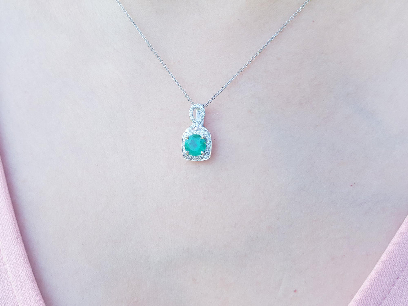 Necklace with a round cut emerald pendant on a person's neck.