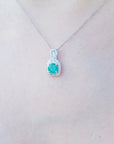 Necklace with a round cut emerald pendant on a person's neck.