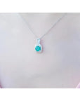 Round Colombian emerald and diamond halo pendant in 18K white gold, worn on a woman's neck.