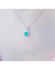 Round Colombian emerald and diamond halo pendant in 18K white gold, worn on a woman's neck.