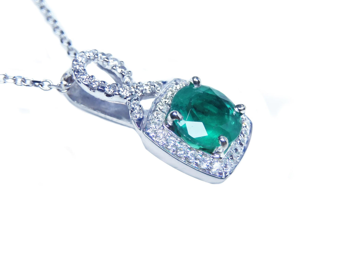 A round cut emerald and diamond pendant in 18k white gold with a chain.