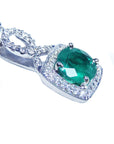 A round cut emerald and diamond pendant in 18k white gold with a chain.