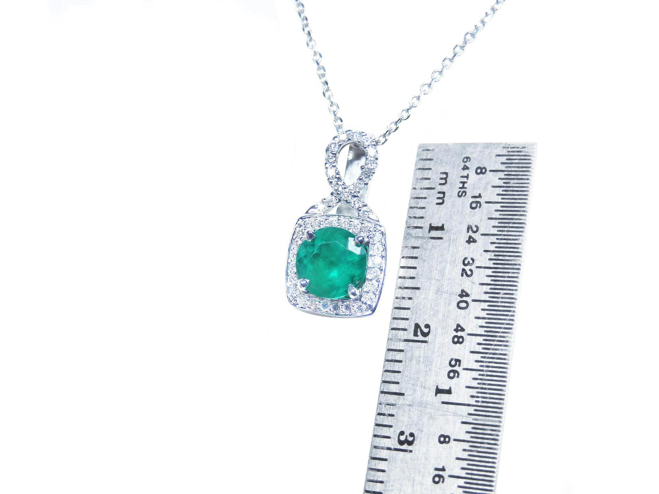 Emerald pendant on a chain with a ruler for scale on a white background