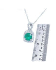 1.08 ct round deep bluish-green emerald and diamond halo pendant in 18K white gold, shown with a ruler.