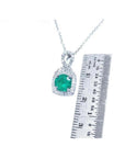 1.08 ct round deep bluish-green emerald and diamond halo pendant in 18K white gold, shown with a ruler.