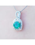 A 18k white gold pendant with a natural colombian emerald on a light pink background.