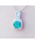 A 18k white gold pendant with a natural colombian emerald on a light pink background.