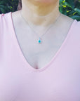 A woman wearing a pink top with a natural emerald pendant necklace against a green leafy background