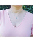 Round Colombian emerald and diamond halo pendant in 18K white gold on a woman's neck.