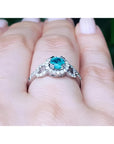 Round cut emerald halo ring with natural diamonds set in 14K white gold on a hand.