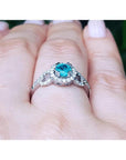 Round cut emerald halo ring with natural diamonds set in 14K white gold on a hand.
