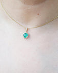 Gold necklace with a round cut natural emerald pendant necklace on a person's neck.