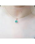 Round cut Colombian emerald pendant necklace with halo diamonds on a 14K gold chain.