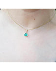 Round cut Colombian emerald pendant necklace with halo diamonds on a 14K gold chain.