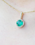 Gold necklace with a round cut natural emerald pendant on a person's neck.