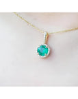 Gold necklace with a round cut natural emerald pendant on a person's neck.